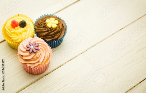 Three swirl frosting cupcakes with candy toppers are sitting on wooden plank in flat design