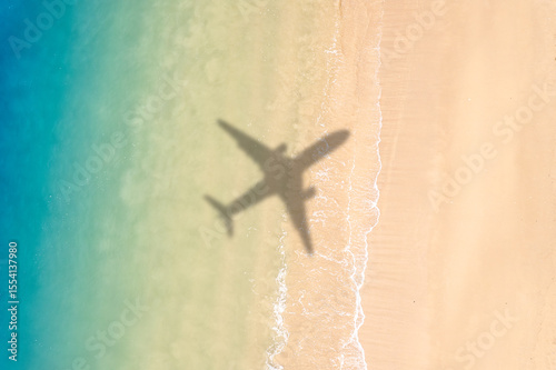Aerial view of shadow passenger plane silhouette and sandy beach blue sea with waves at sea beach summer vacation sea travel concept	
