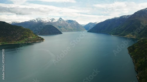 Hardanger fjord demonstrates deep blue waters flanked by majestic mountains under cloudy sky. Dramatic landscape highlights serene beauty of Norway