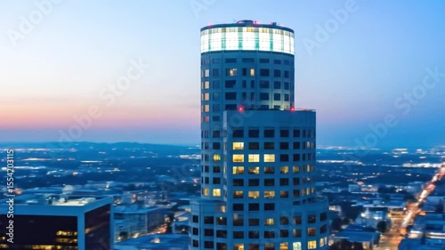 A modern highrise tower glows brightly against the night sky overlooking a sprawling city with twinkling lights below