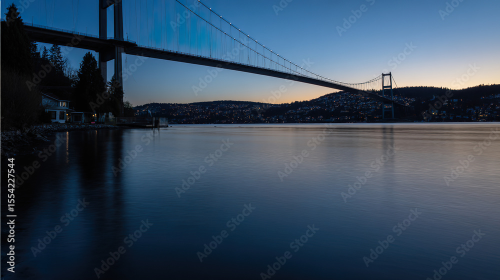 Obraz premium Suspension bridge in twilight, reflections on water, long exposure. Urban serenity meets timeless structure.