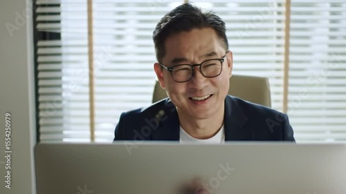 Joyful Asian Business Professional Smiling and Laughing While Working on Laptop in a Modern Office