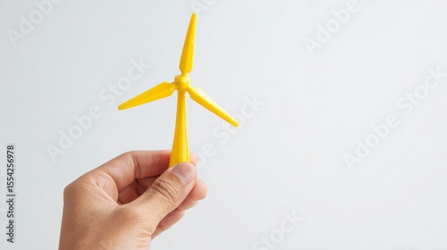 Hand Holding a Small Yellow Wind Turbine Model for Renewable Energy Concept on White Background