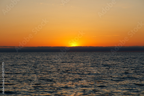 The sun is setting over the ocean, casting a warm glow on the water