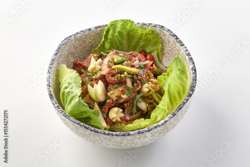 Bowl of spicy raw chopped beef salad garnished with fresh herbs, garlic, and vegetables, served on bed of crisp lettuce leaves in ceramic bowl, showcasing vibrant colors and textures