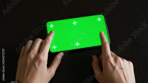 Hands Using Smartphone with Green Screen Display 4K Top view of two fingers interacting with a smartphone screen featuring a green screen placeholder