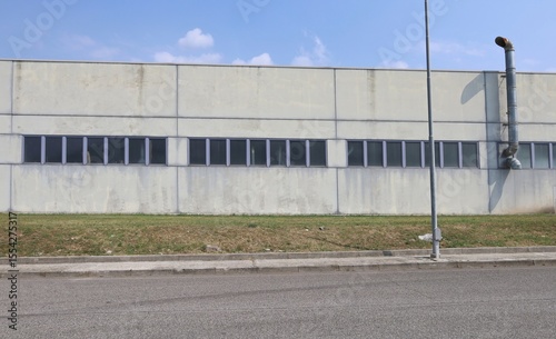 Wallpaper Mural Concrete facade of factory building with row of window and a chimney. Meadow, sidewalk and road in front, sky above. Background for copy space. Torontodigital.ca