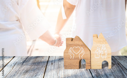 Nursing home service concept, miniature house on wood floor over blurred girl holding hand crossing the bridge, health care and elderly care