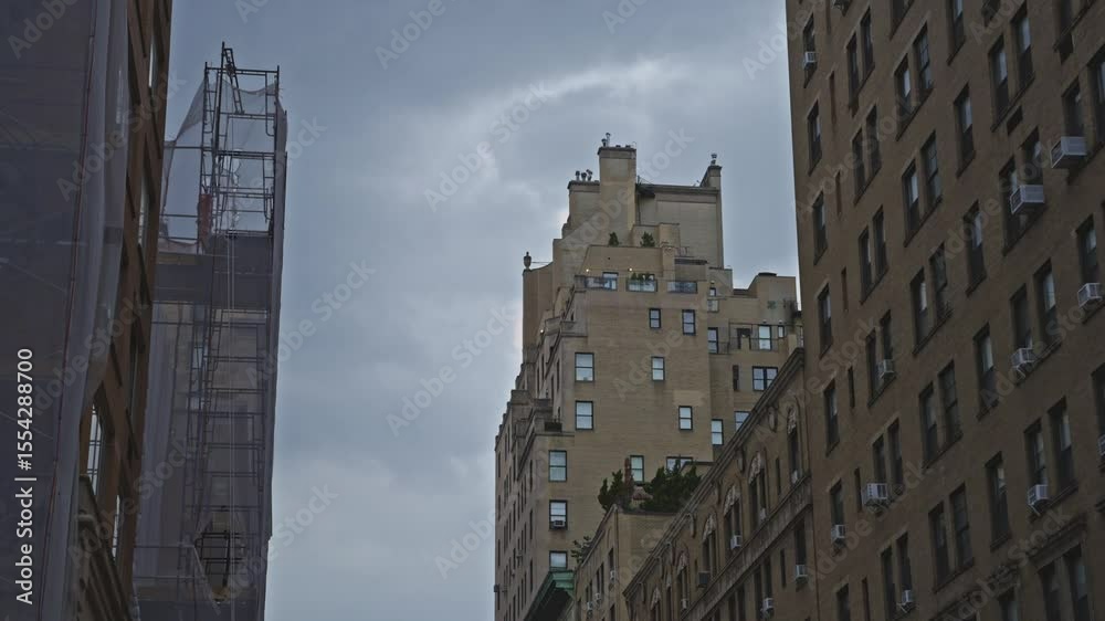 View of a luxury tiered apartment building in NYC’s Upper East Side, framed between older brick buildings and wrapped scaffolding, under a moody overcast sky. View of a luxury tiered apartment building in NYC’s Upper East Side, framed between older brick buildings and wrapped scaffolding, under a moody overcast sky.