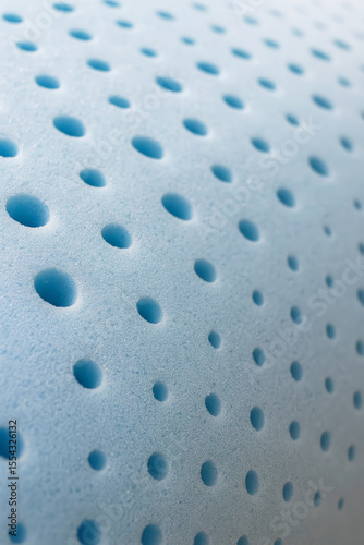 Close-up of perforated blue memory foam with evenly spaced round holes. The surface is soft, porous, and smooth with a subtle matte finish. The light falls diagonally