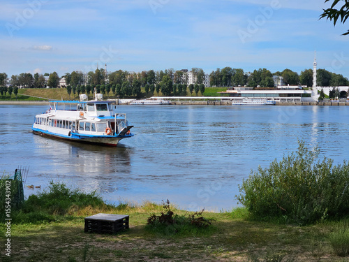 Boat is traveling on a river Volga in Yaroslavl. The boat is blue and white. There are several other boats in the water and river port for passengers