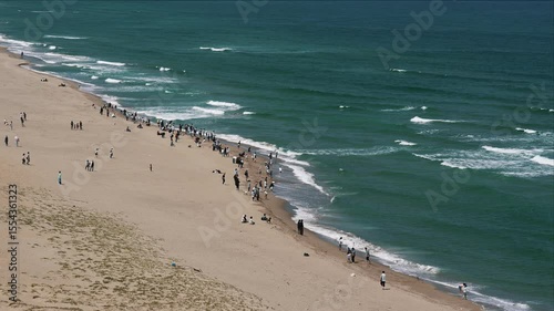 Expansive sandy beach with ocean waves many people enjoying day.
