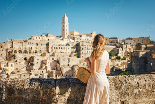Woman tourist enjoying panoraming view of Matera city in Italy.Young woman in romantic dress and handbag standing against the backdrop of ancient city of Matera in Italy