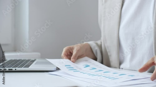 Professional businesswoman analyzing financial reports and graphs, examining data insights for strategic corporate planning in modern workplace setting. Business people concept