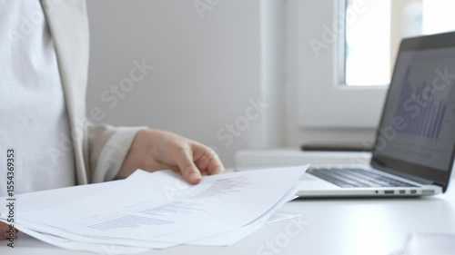 Businesswoman reviewing financial documents and analyzing data on charts and graphs while working at her desk with a laptop. Business people concept