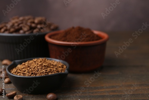 Different types of instant coffee and beans in bowls on wooden table against brown background, closeup