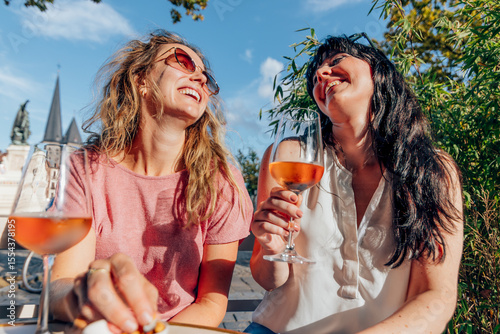 Two female friends enjoying wine and laughing together outdoors in summer