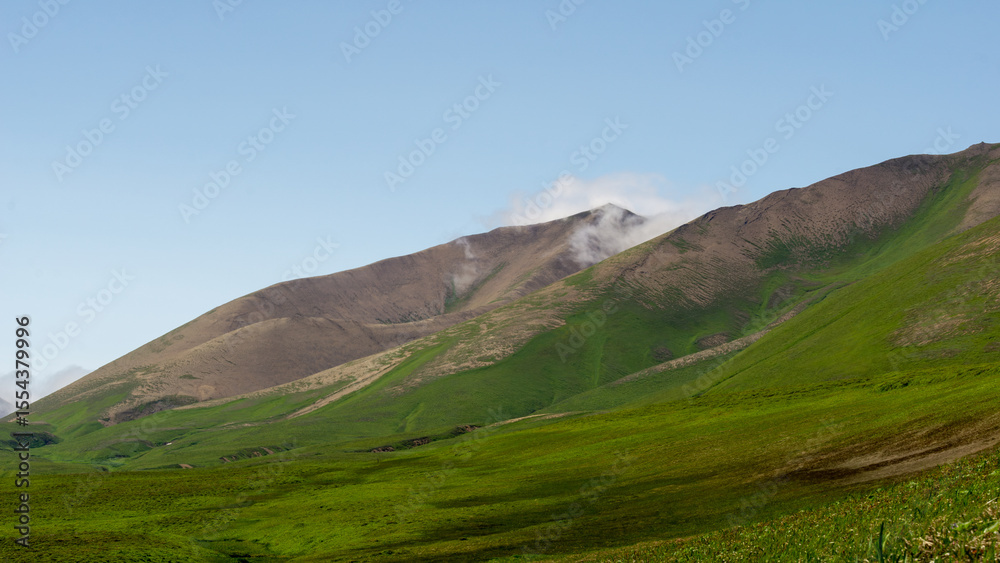 Obraz premium Majestic green hills under a clear blue sky, with gentle slopes and distant mountains, showcasing the beauty of nature and serene landscape in a tranquil environment