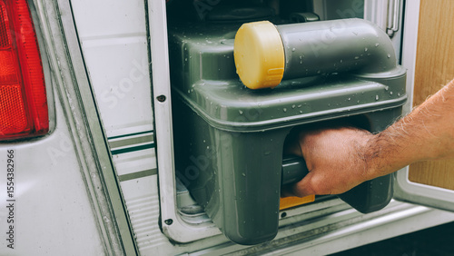 Man's hand serving caravan, tank toilet cassette in dump point during road trip. Dumping station for recreational vehicle. Camper service.