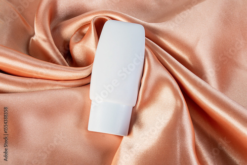 Cosmetic product in tube, bottle, lotion or serum on shiny cloth background