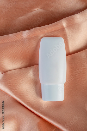 Cosmetic product in tube, bottle, lotion or serum on shiny cloth background