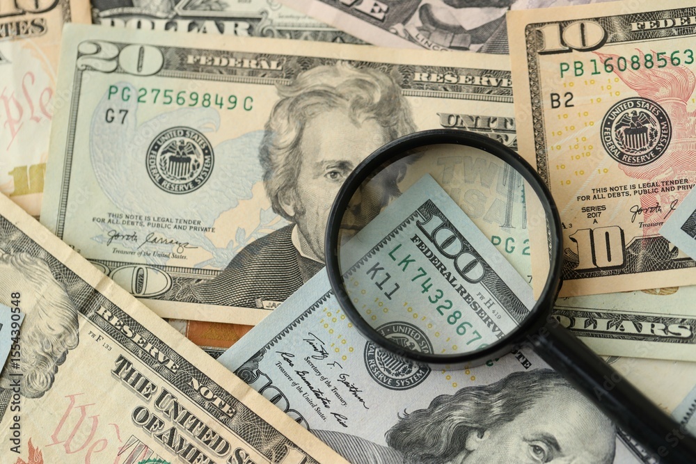 Big amount of United States USD dollar bills and magnifying glass