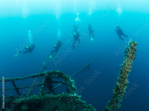 divers diving next to the wreck of a sunken ship in the sea colonized by marine life, concept of scuba diving and underwater adventure