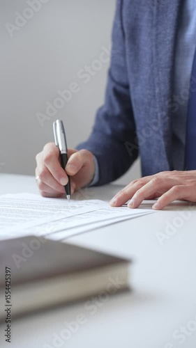Close up of businessman's hands signing a contract with elegant pen, wearing a blue suit and a wristwatch, sitting at a white desk. Business people concept