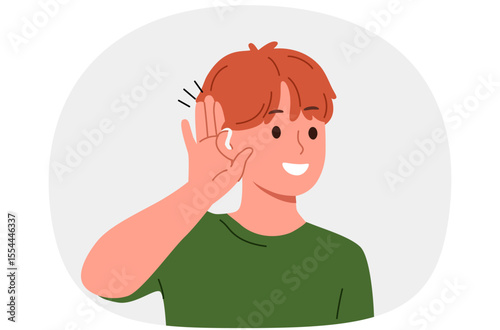 Boy uses hearing aid and puts palm to ear, rejoicing at availability of technological solutions to health problems. Schoolboy with hearing aid smiles listening to sounds around him.