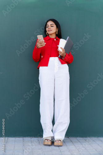 Woman texting and holding laptop and coffee outdoors