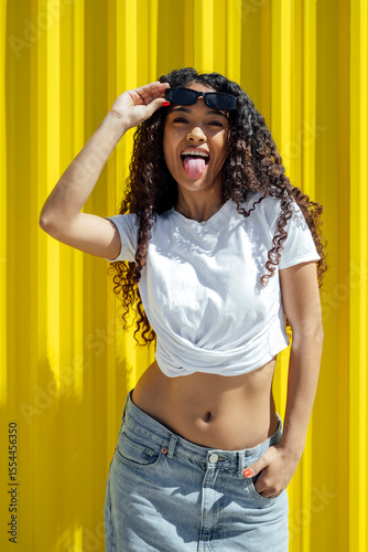 Playful woman with curly hair wearing sunglasses on yellow background