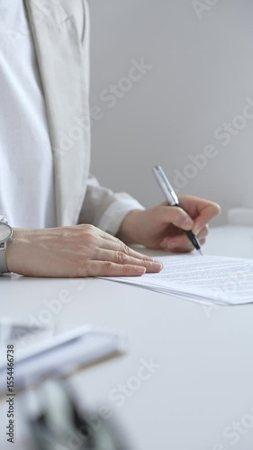 Businesswoman signing a contract at her office desk, surrounded by a laptop and documents, exemplifies focus and commitment. Business people concept