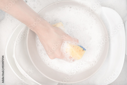 Female hand with sponge for washing dishes and bowls in water with foam or dishwashing liquid. washing dishes in the sink