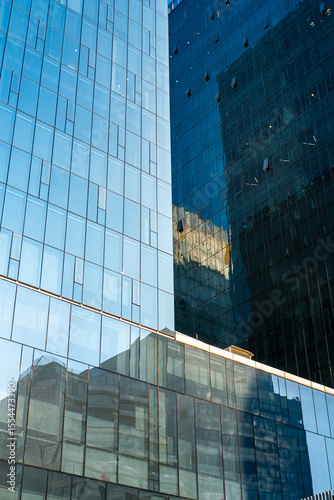 Tall blue skyscrapers reflected in glossy glass surfaces creating vertical urban patterns, elegant architectural details and modern geometry under bright contemporary daylight.