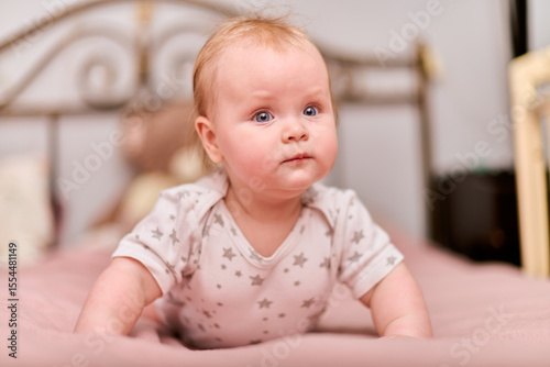Young female child with light hair, playful expression, star-patterned pajamas. Pink bedding, blurry teddy backdrop, soft lighting, cozy home setting, warm atmosphere