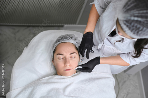 Young woman receives calming facial treatment in modern spa clinic. Serene ambiance, emphasized by white towels and gloves, promotes relaxation and skincare rejuvenation