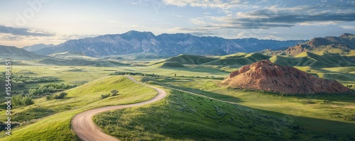 A winding dirt road cuts through lush green hills under a partly cloudy sky with distant mountains in the background.