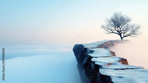 A solitary tree stands on a snowy cliff edge overlooking a misty, serene landscape under a pale blue sky at dawn or dusk.