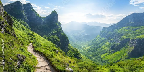 A scenic mountain trail winds through lush green valleys and towering peaks under a clear blue sky with the sun shining brightly.