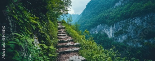A stone staircase ascends through lush greenery in a mountainous forest landscape under a cloudy sky.