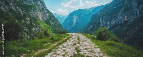 A rugged stone path winds through lush green mountains under a bright sky, offering a serene and scenic natural landscape.