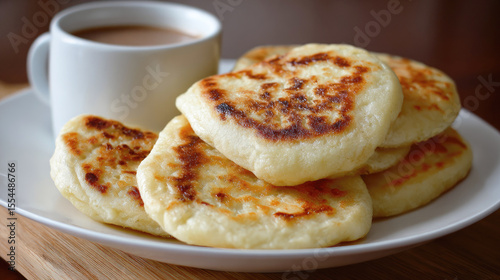 Golden cheese pancakes served on a white plate with a hot drink, creating a cozy and appetizing breakfast scene in warm natural light.