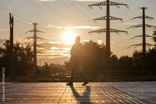 Woman walking on background of high voltage towers with electrical wires. Electricity transmission lines in city at sunset