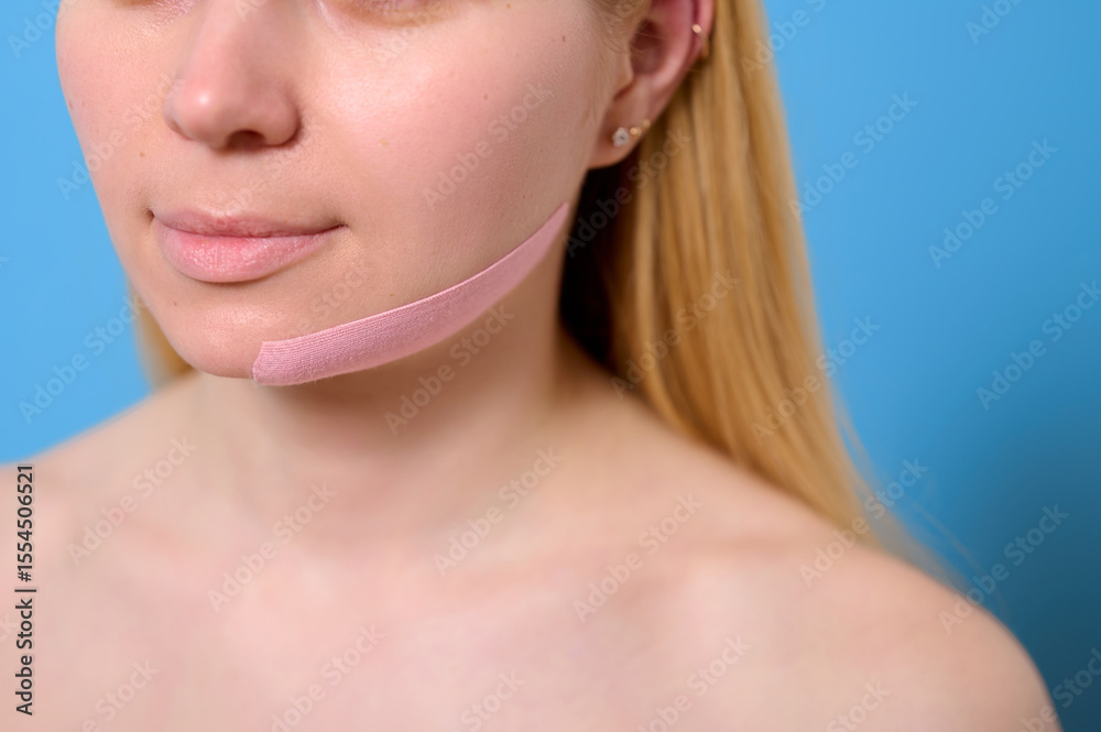 Obraz premium woman with facial lifting tape against blue background. close-up of innovative beauty trend for skin tightening and anti-aging. modern self-care and facial sculpting technique