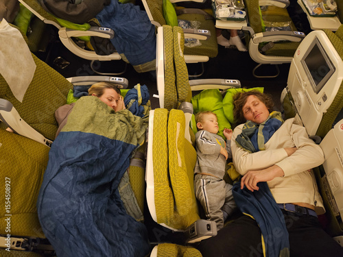 Man and a child are sleeping on a plane. A woman is sleeping on the other side of the plane. father and mother