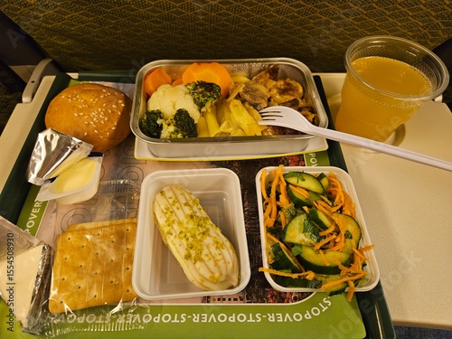 Tray of food with a fork and a cup of juice. The tray has a sign that says Stopover Superstore in airplane