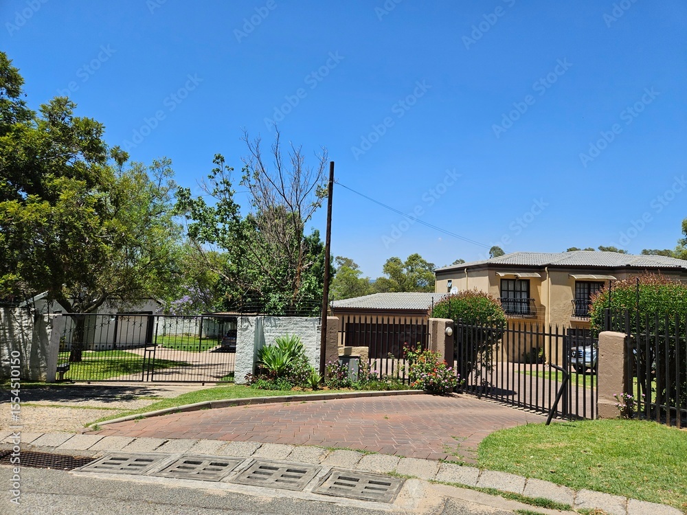 Obraz premium House with a gate and a driveway. The gate is black and the driveway is red. The house is on a street with a sidewalk in Johannesburg in South Africa