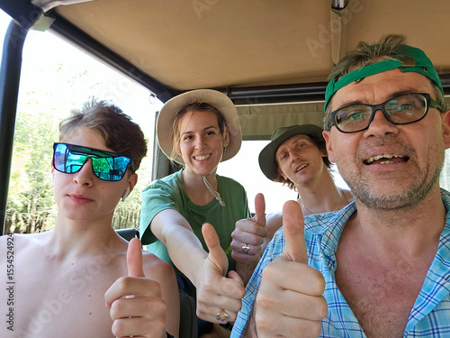 Man and three friends are in a vehicle, with the woman wearing a green shirt and two man with glasses with OK gesture during safari in park in South Africa