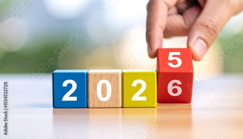 Hand adjusting a red block to show the year 2025 using colorful wooden toy blocks on a surface