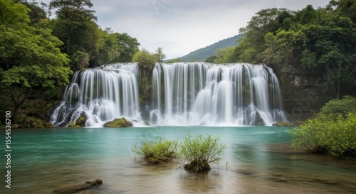 Beautiful cascading waterfall surrounded by lush green forest and turquoise water